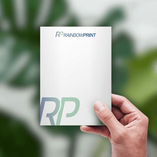 Ein DIN A4 Flyer von Rainbowprint, der in einer Hand gehalten wird.