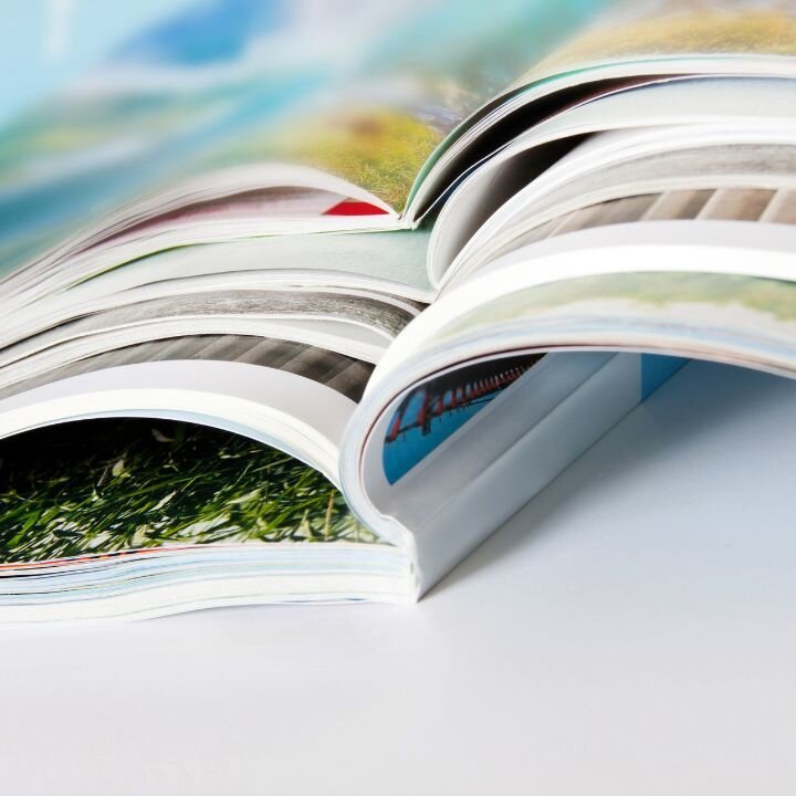 Verschiedene Broschren mit Klebebindung, die aufgeschlagen aufeinander liegen.