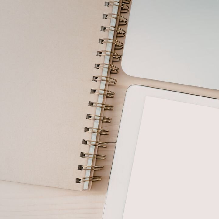 Ein Block mit Spiralbindung auf einem Schreibtisch. Daneben ein Laptop.