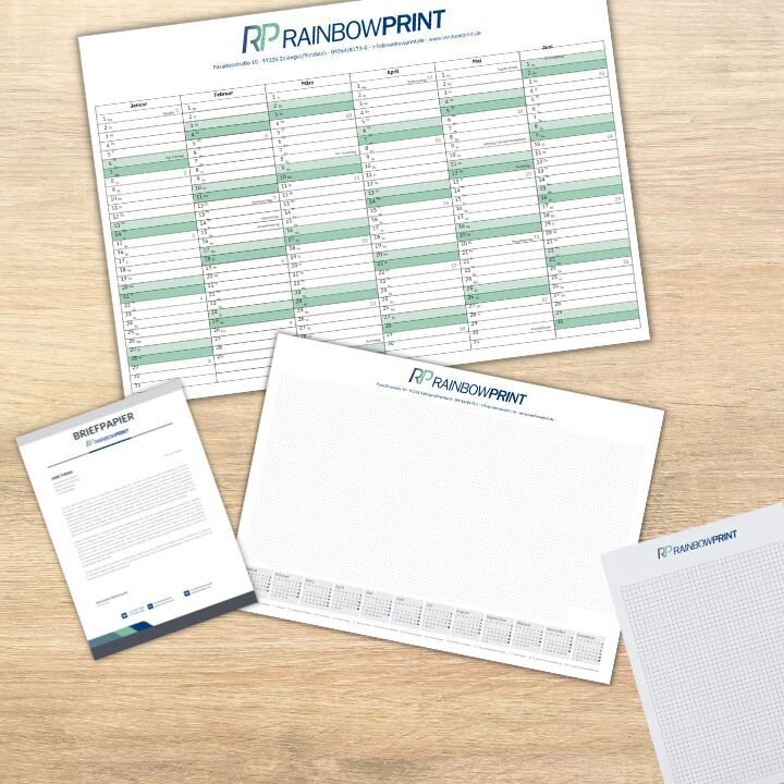 Verschiedene Geschftsausstattung gedruckt von Rainbowprint auf einem Holztisch. Darunter ein Kalender, Briefpapier und ein Block.