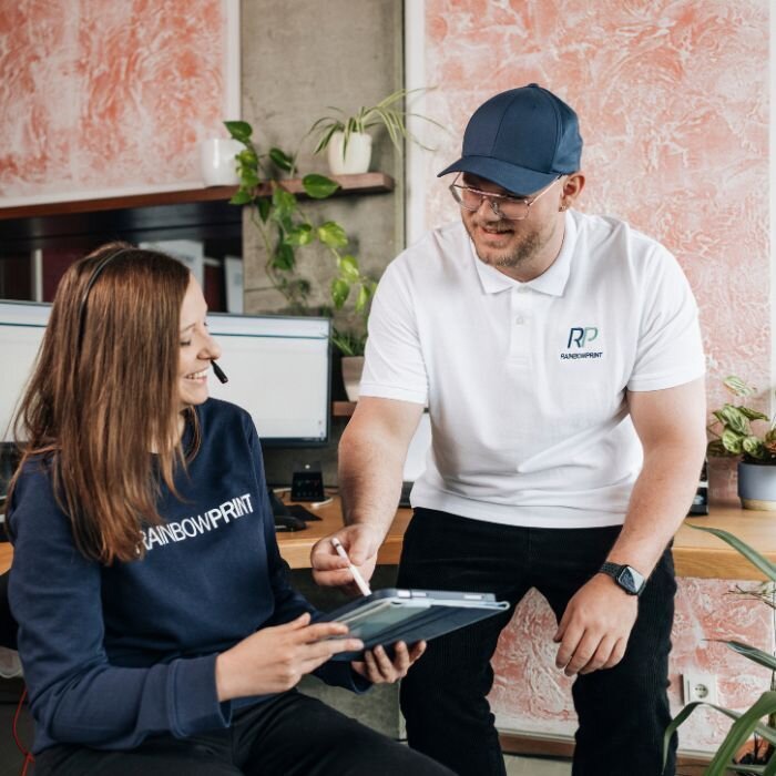 Ein Mitarbeiter von Rainbowprint, der einer Kollegin auf einem Tablet etwas zeigt.