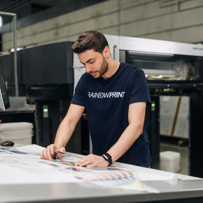 Ein Mitarbeiter von Rainbowprint, der an der Druckmaschine steht und eine Sichtprfung vornimmt.