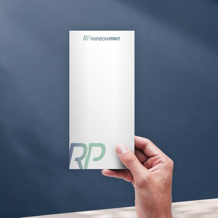Ein Flyer von Rainbowprint, welcher von einer Hand ins Bild gehalten wird im Format DIN Lang.